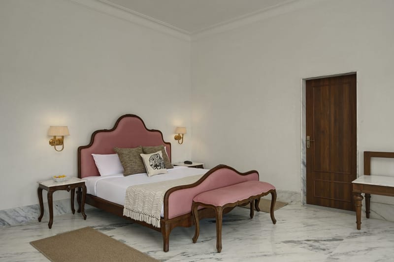Suite bedroom with a pink upholstered bed, wall lamps, and a wooden door