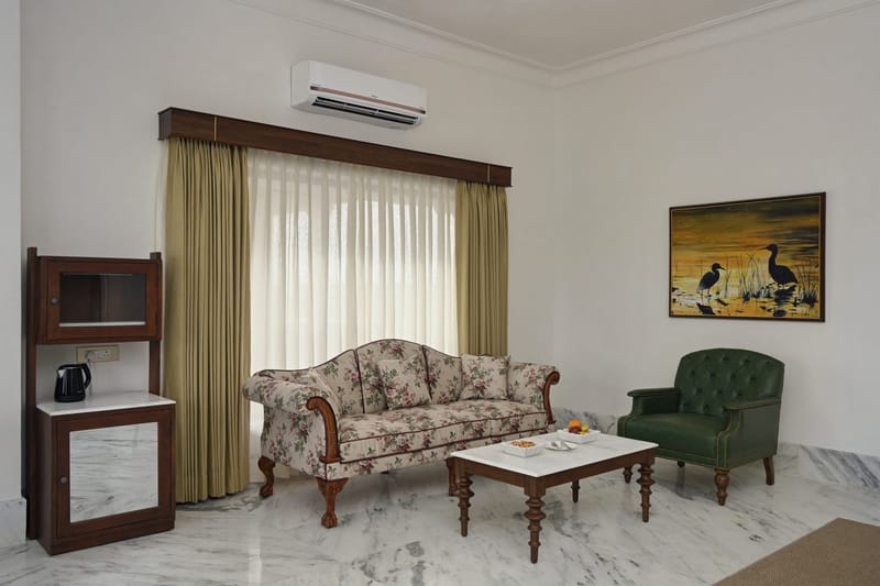 Suite living room with floral sofa, green armchair, marble table, and minibar cabinet