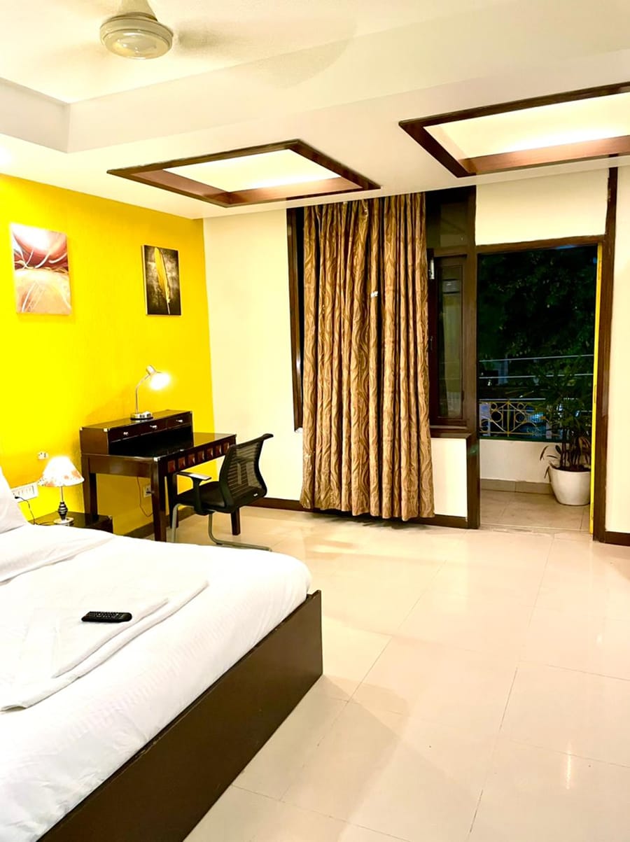 Bedroom with a yellow accent wall, writing desk and balcony access at Lime Tree, Greater Kailash-2