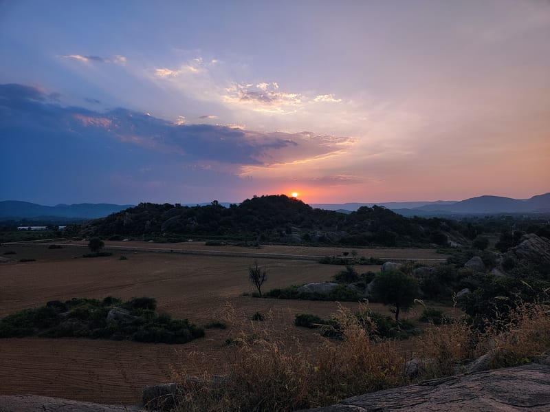 A picture featuring a range of mountains and sunset, with both dry and green land