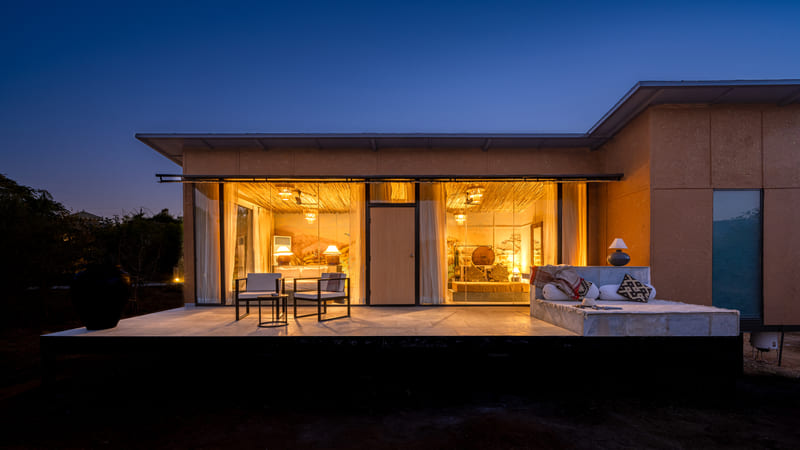 A villa lit from within at dusk, seen across its deck