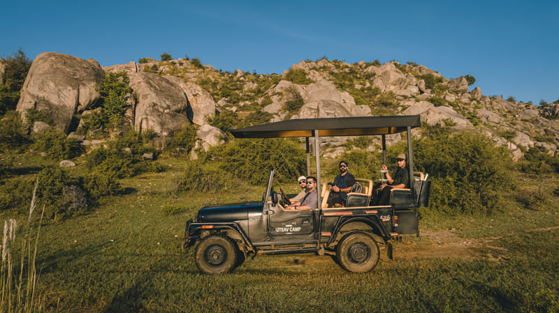 A group of people on a safari jeep with a hill in the background - Utsav Camp Sariska