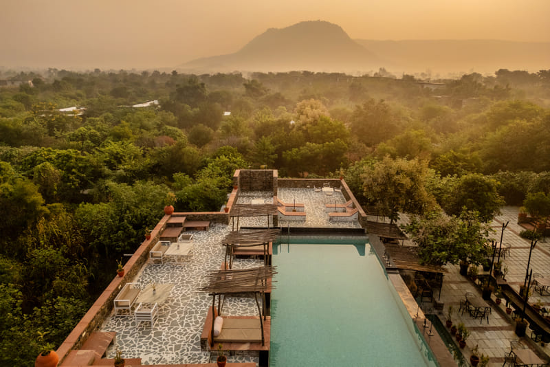Aerial view of a swimming pool, surrounding forest cover and a mountain in the background at Utsav Camp Sariska.