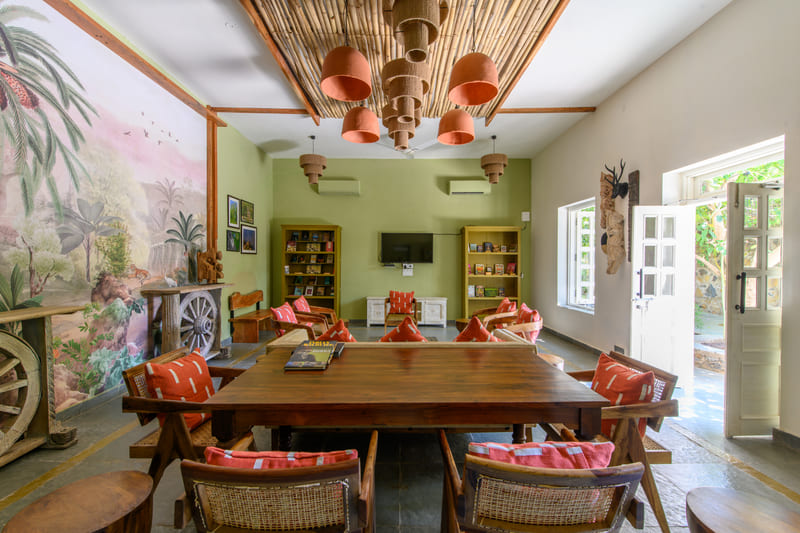 A cosy lounge and library room at Utsav Camp Sariska with wooden furniture, bookshelves, and wildlife wall art.