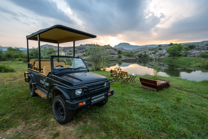A safari jeep and picnic seating beside a still pool at dusk