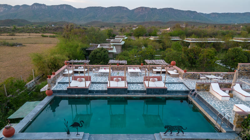 Aerial view of an outdoor swimming pool with lounge chairs and shaded daybeds at Utsav Camp Sariska.