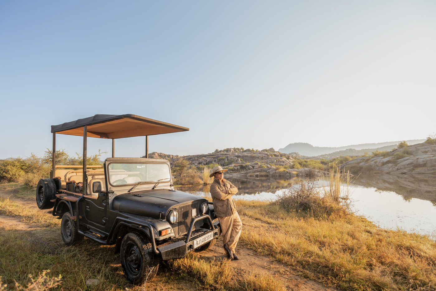 A safari jeep parked by the water, a guide scanning the far bank