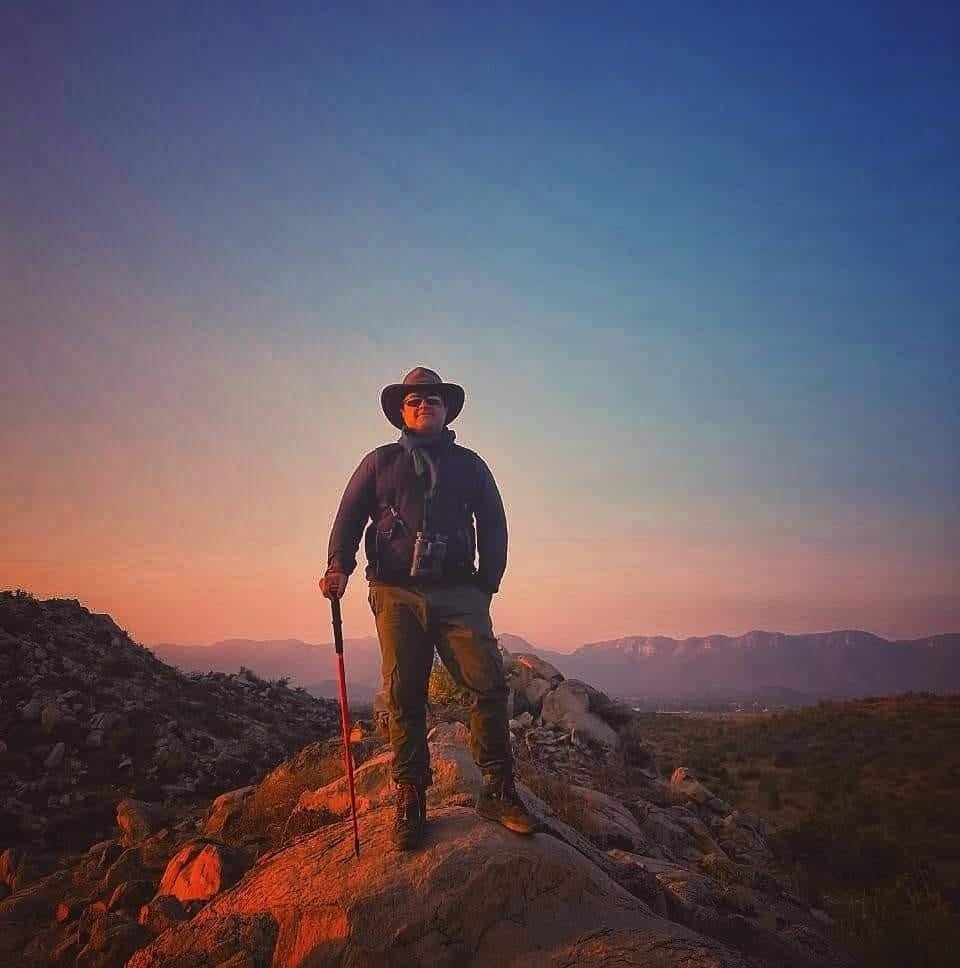 An image of a person standing on a hilltop with a dusky sky as the backdrop