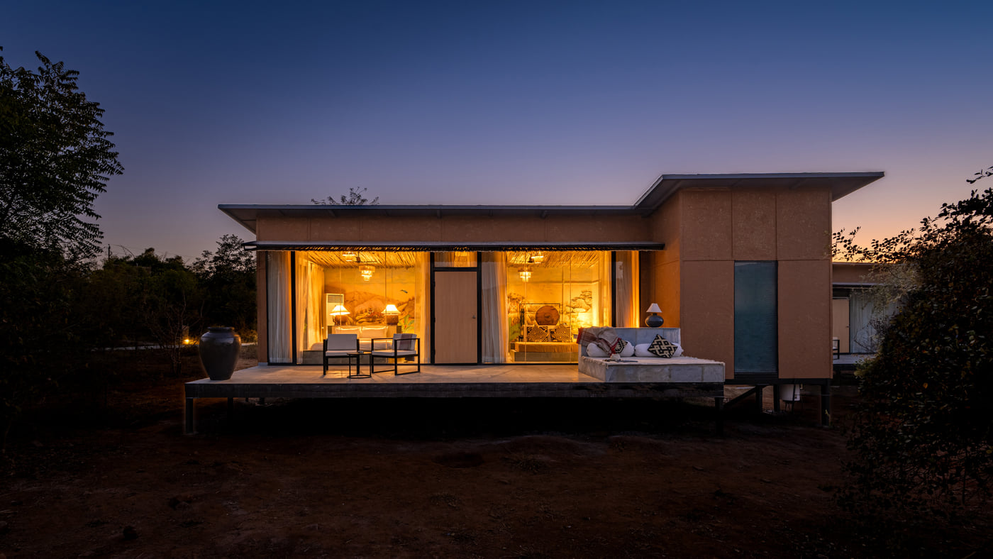 A facade view of a room with bright lighting and greenery around - Utsav Camp Sariska.
