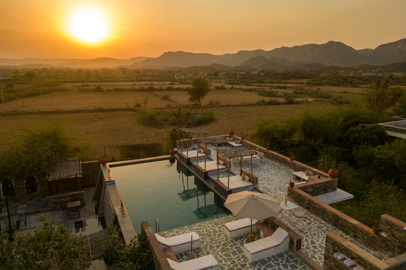 A serene sunset seen in the shot with a roof top swimming poll below it - Utsav Camp Sariska