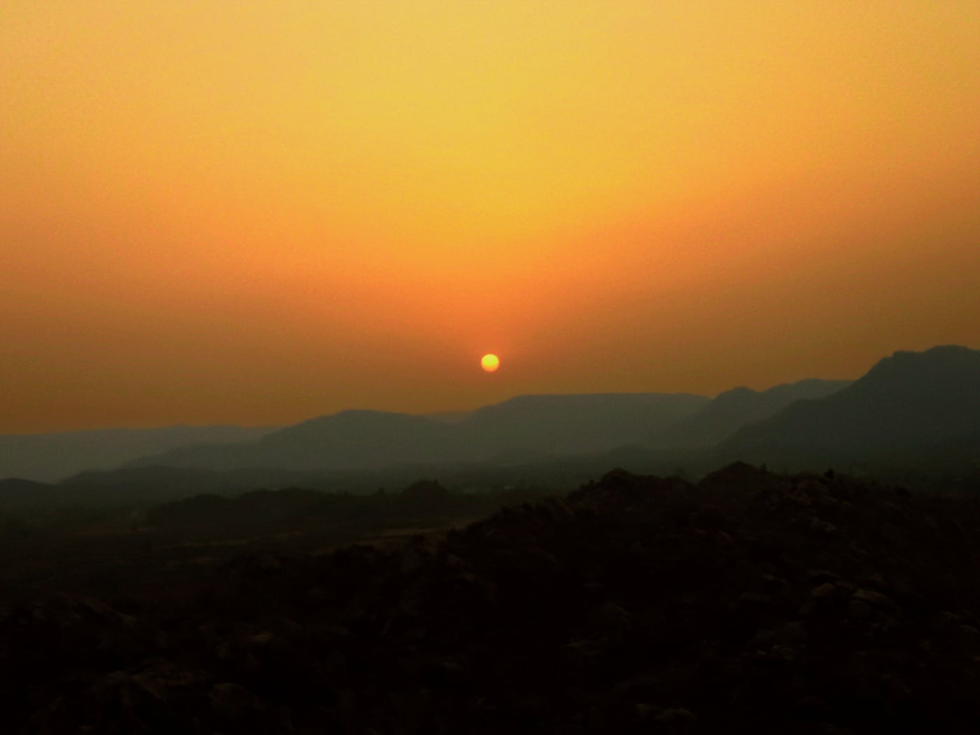 Sunset over rolling hills and mountain silhouettes in the wilderness.