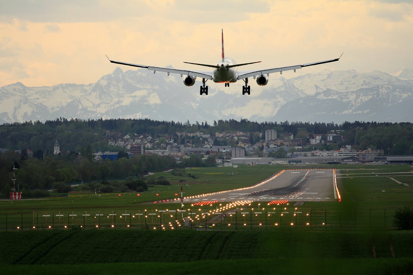 An aeroplane landing on a runway with grass on either side of it.