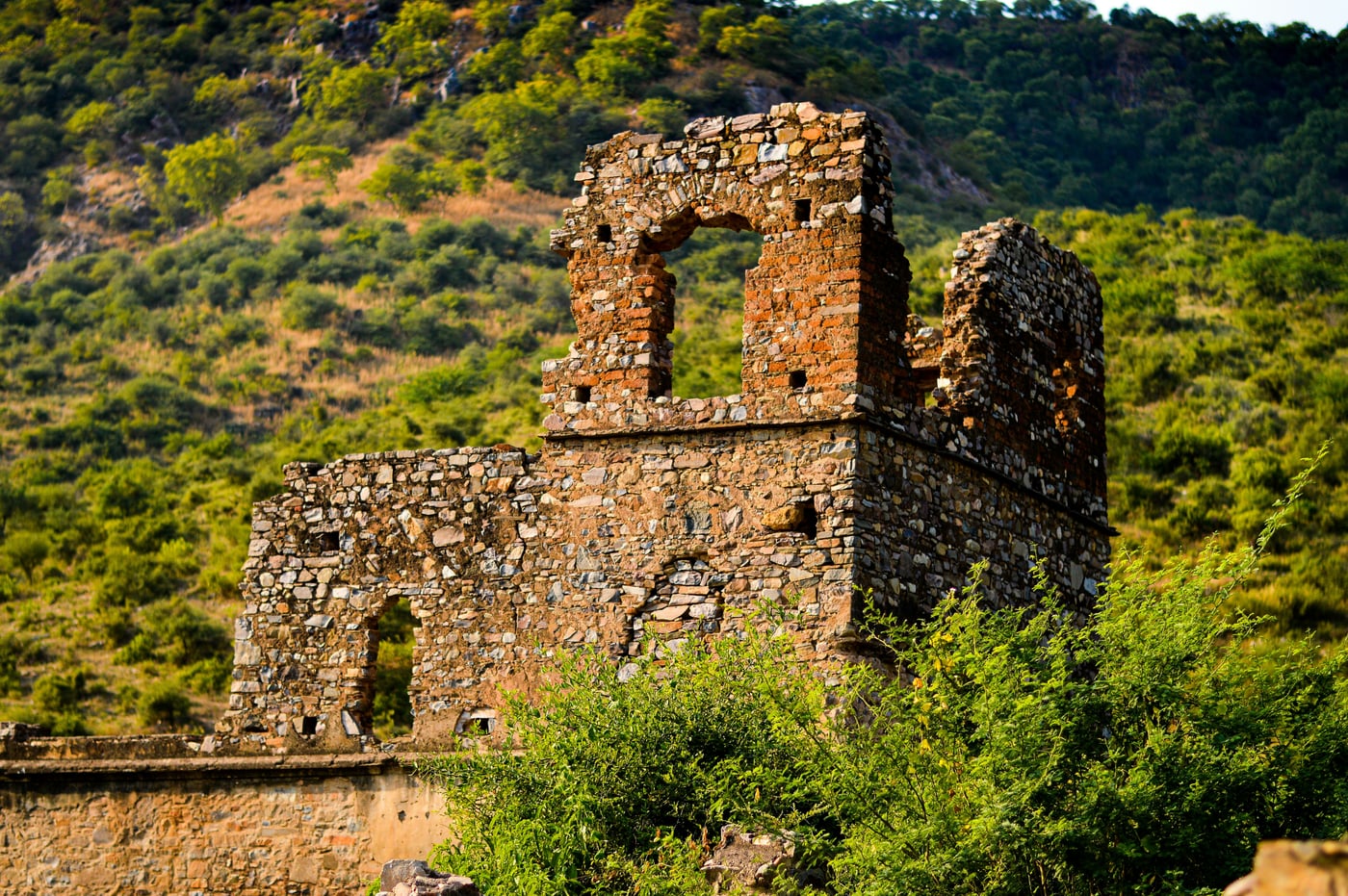 A structure made out of stone in Bhangarh Fort with greenery in the background.