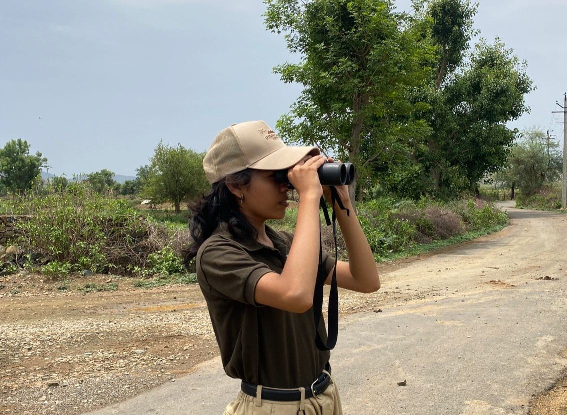 A birder using binoculars to observe wildlife and bird species across the open landscapes surrounding Utsav Camp Sariska.