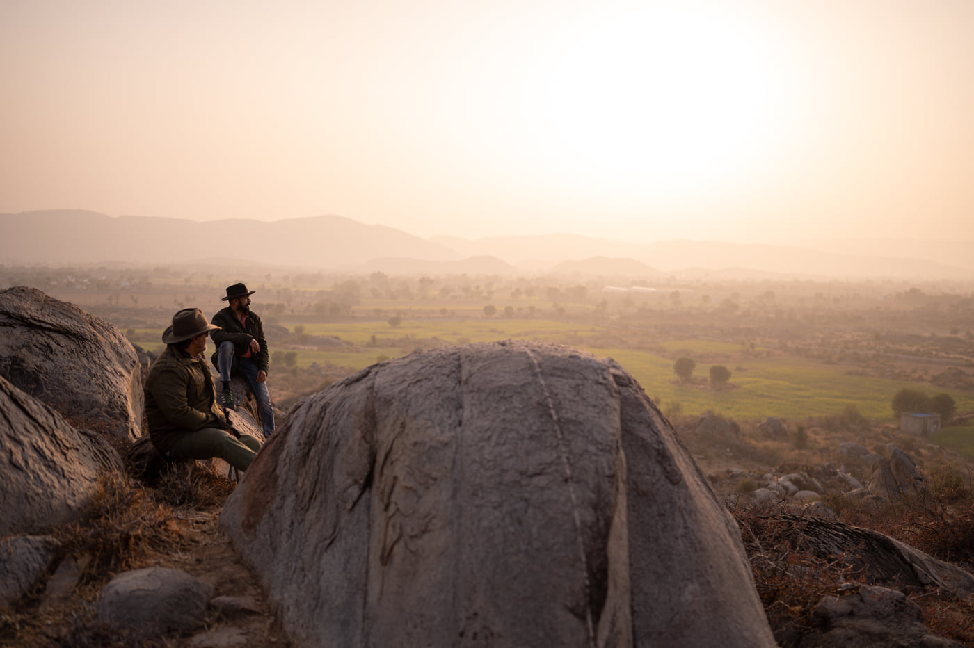 Two people sitting out on a boulder as the sun drops