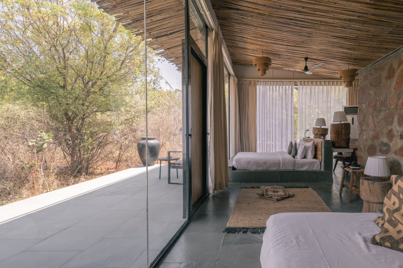 Inside a Forest Bungalow, the bed facing a full-height glass wall onto the forest