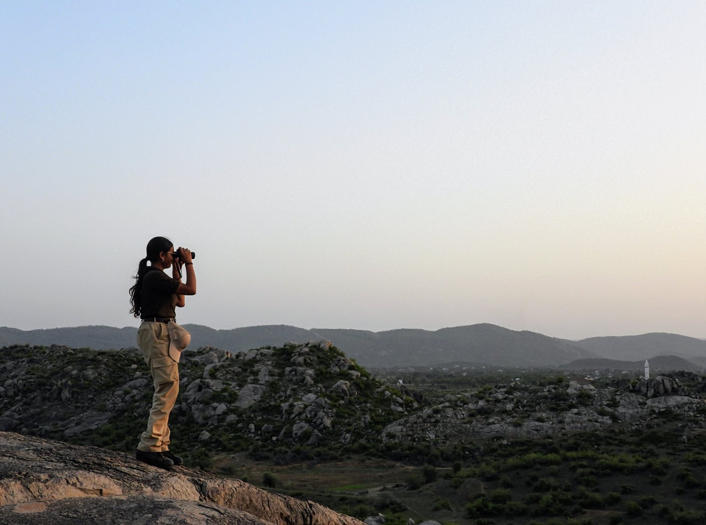 Wildlife photographer standing on a rocky hill capturing nature with a camera.