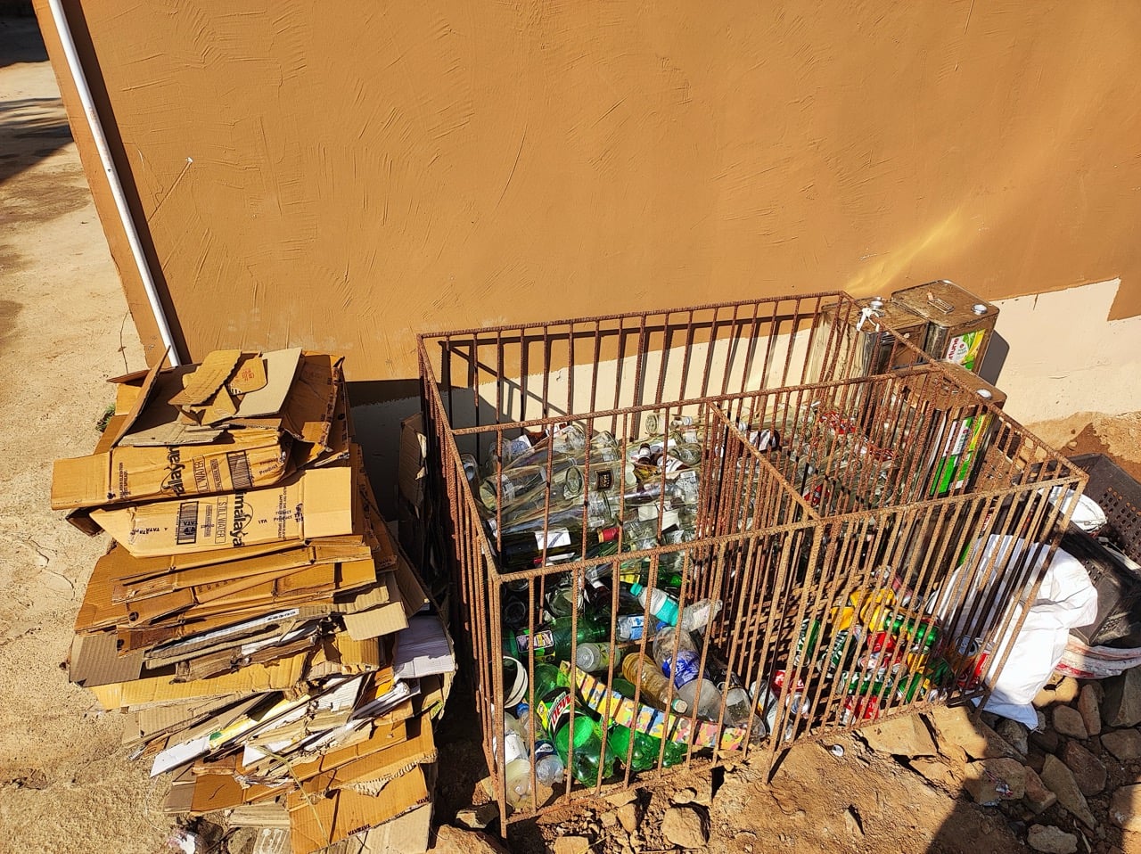 Flattened cardboard and a wire bay of sorted glass and plastic at the camp