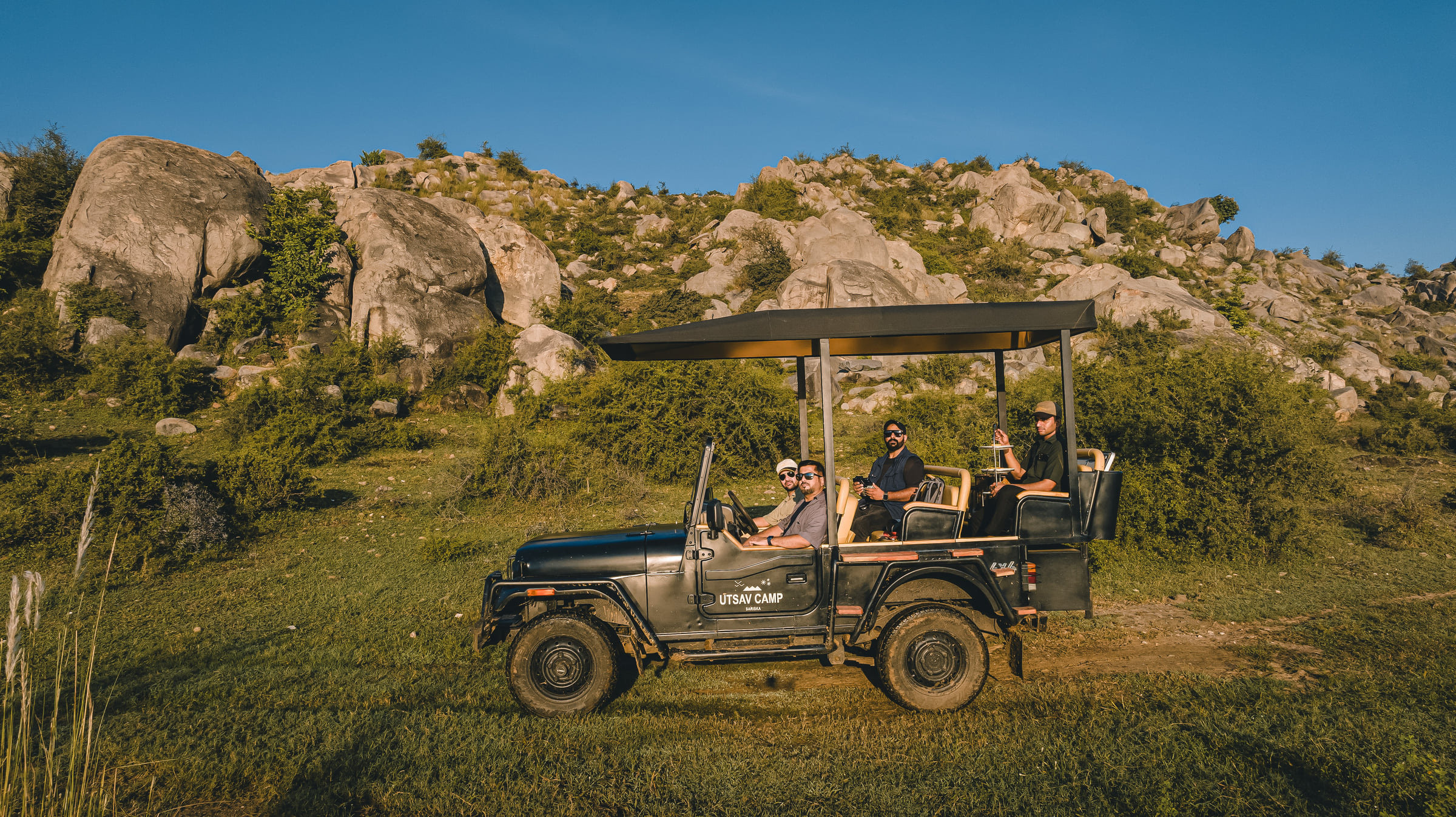 A group of people on a safari jeep with a hill in the background - Utsav Camp Sariska