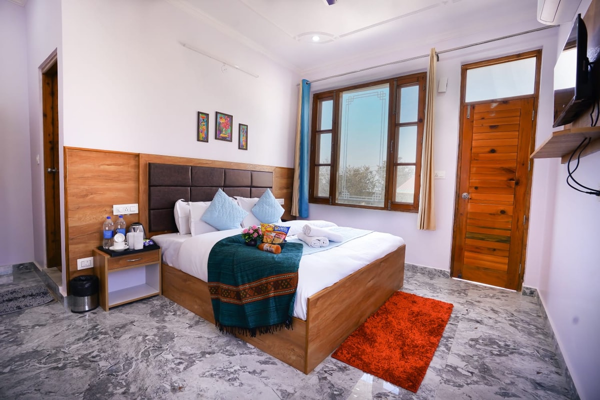 Deluxe Room interior at Hotel Sparrow Dharamshala showing comfortable bedding, balcony door and smart TV