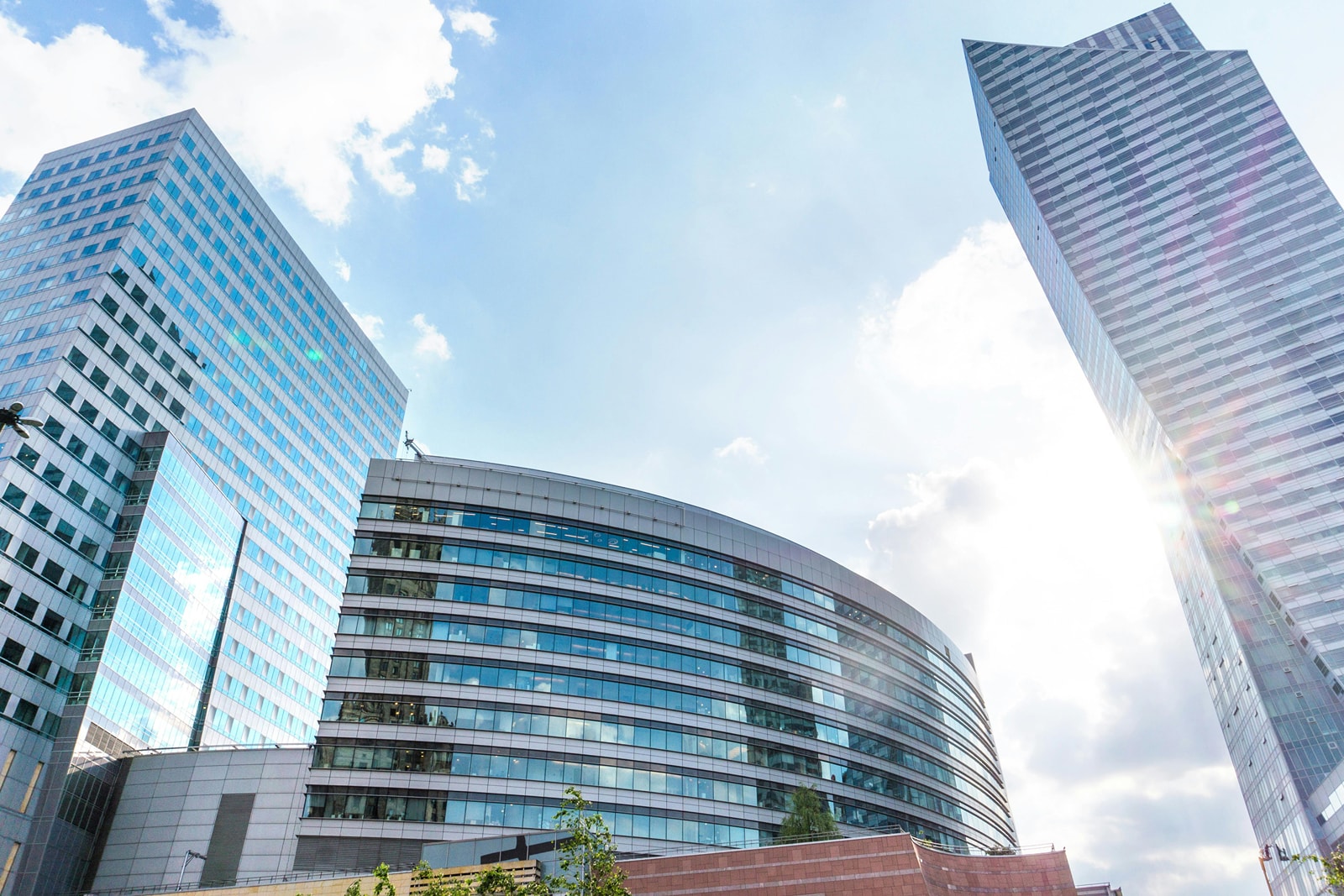 Curved glass-fronted office building beside a tall tower under a bright sky