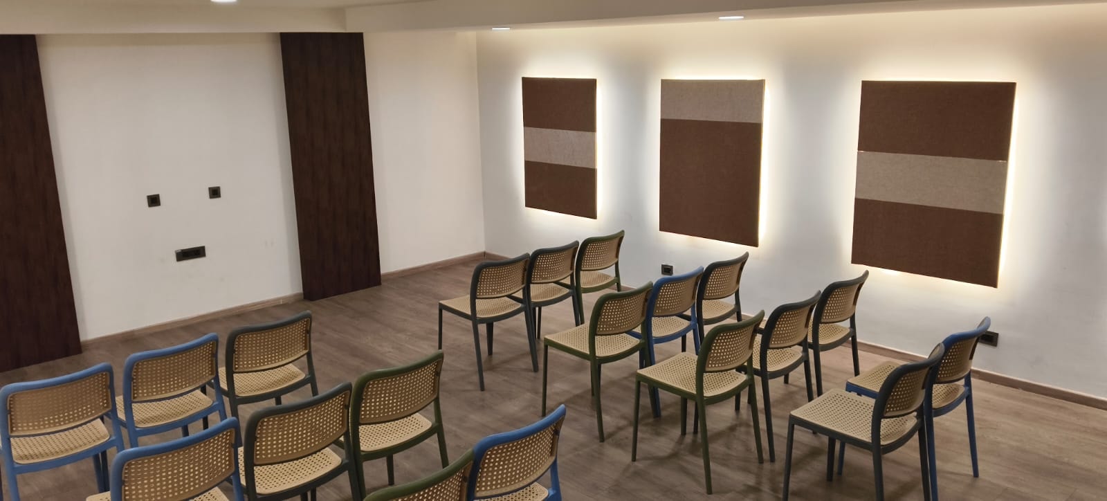 The air-conditioned banquet hall set theatre-style with cane chairs beneath illuminated acoustic wall panels at Rossedale Suites & Hotel in Peelamedu, Coimbatore