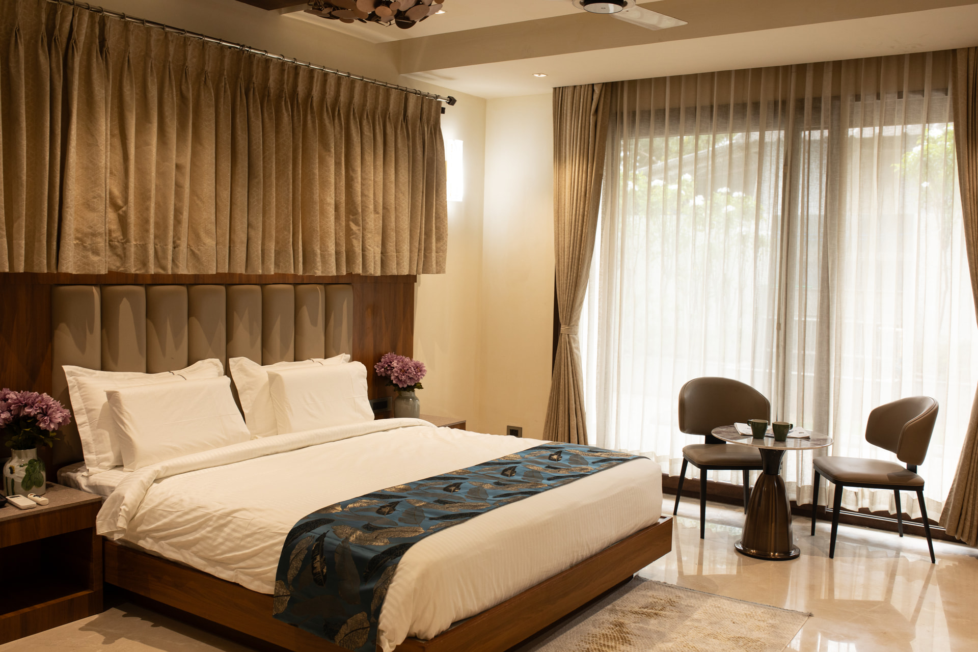 A king bed beside floor-length drapes and a window in an Executive Kitchenette at Rossedale Suites & Hotel in Peelamedu, Coimbatore