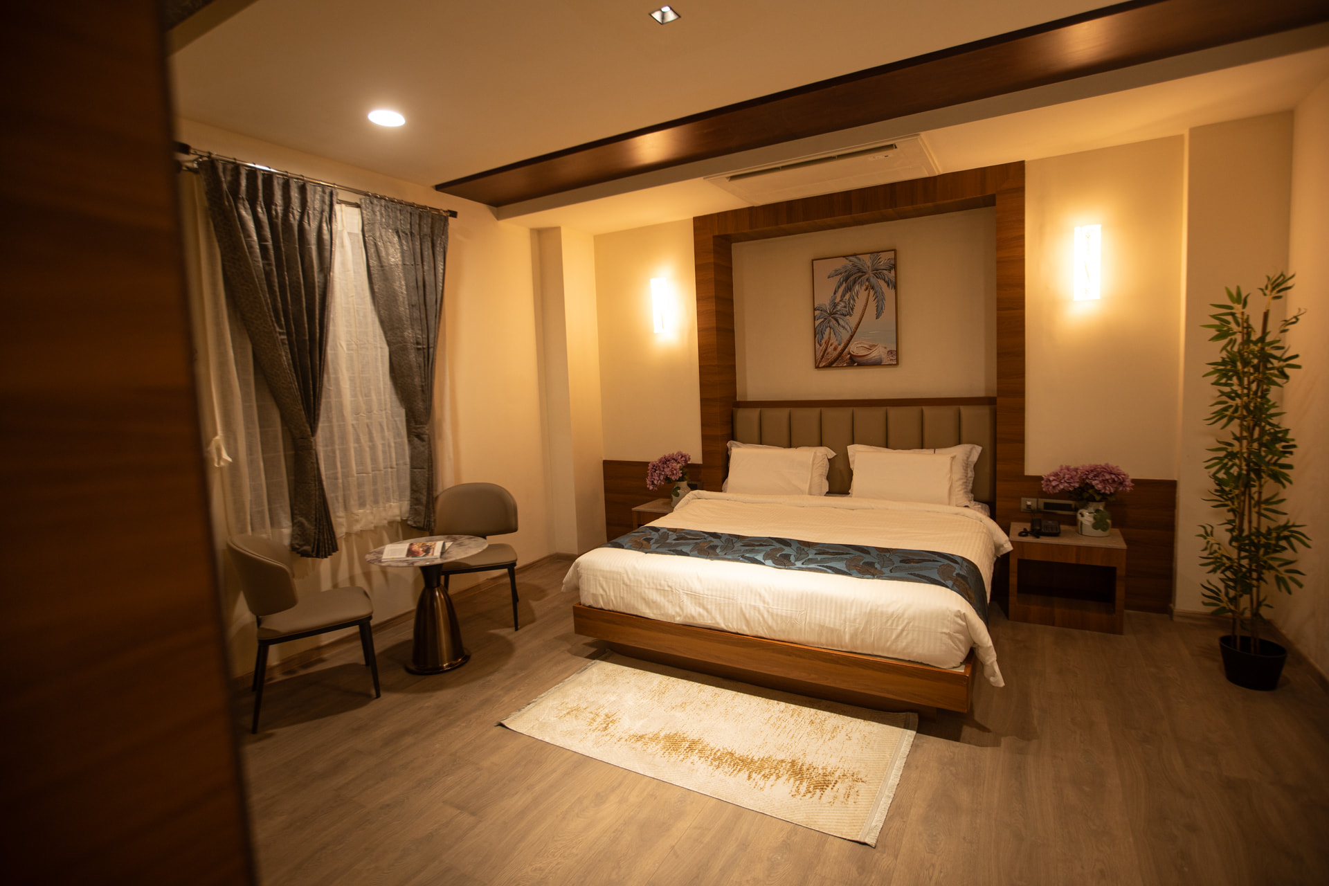 A neatly made king bed and a cushioned lounge chair beside soft drapes in an Executive Room at Rossedale Suites & Hotel in Peelamedu, Coimbatore