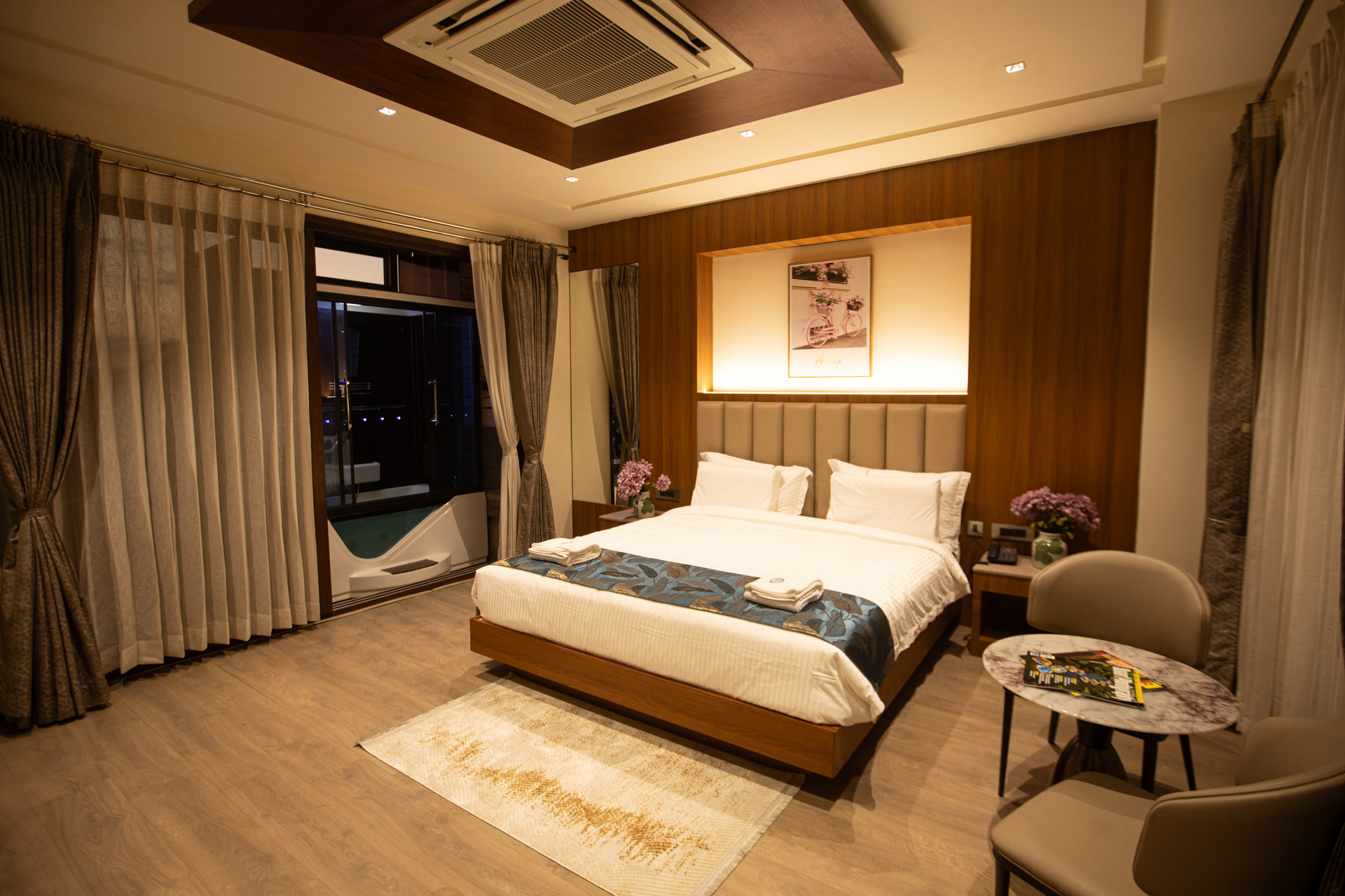 A private in-room jacuzzi set behind a glass partition with blue mood lighting in the Jacuzzi Room at Rossedale Suites & Hotel in Peelamedu, Coimbatore