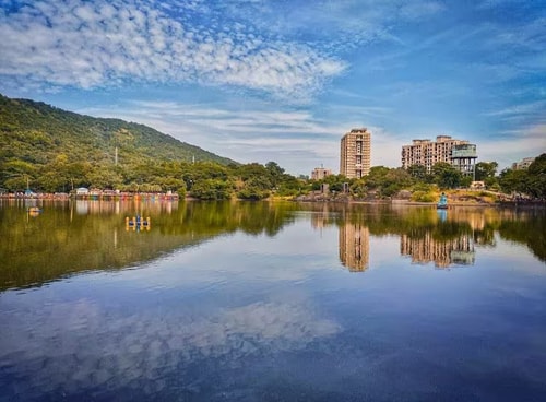 A serene lake, a hill with green trees, and an area with high raise buidlings.