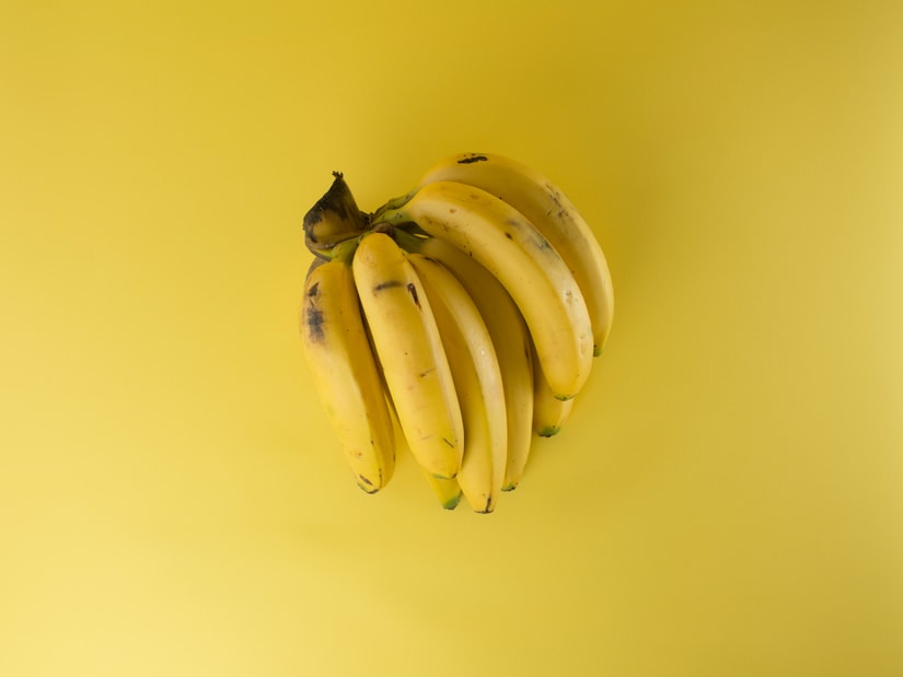 A bunch of ripe yellow bananas with a few dark spots, photographed from above on a yellow background