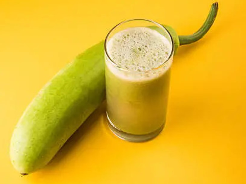 A whole ash gourd beside a tall glass of pale green ash gourd juice on a yellow background
