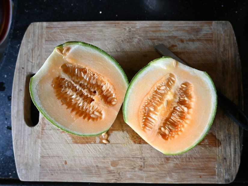 Two halves of a ripe musk melon (cantaloupe) on a wooden cutting board, showing the orange flesh and seed cavity