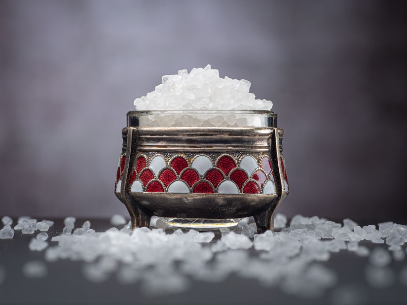 Clear badam pisin crystals heaped in an ornate silver bowl, with more crystals scattered on a dark surface