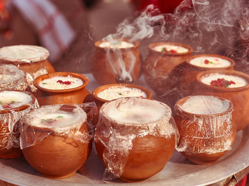 Clay cups of buttermilk topped with cream and covered in plastic wrap, arranged on a metal tray with wisps of smoke rising