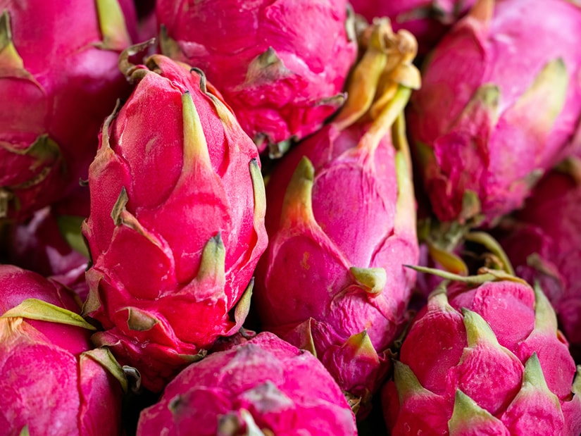 Ripe pink dragon fruit piled closely together, their green-tipped scales overlapping