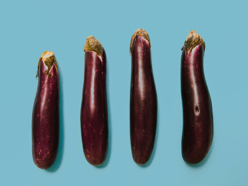 Four whole purple eggplants lined up on a light blue background