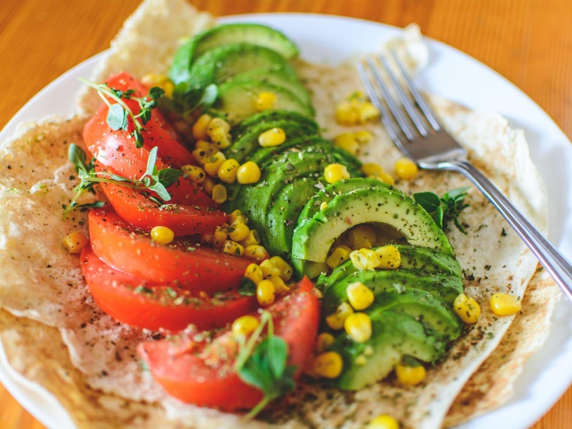 Sliced avocado, tomato wedges, sweetcorn and fresh herbs on a flatbread on a white plate