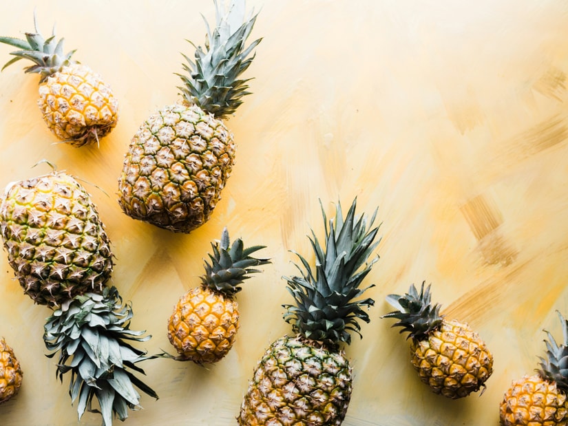 Whole pineapples of varying sizes arranged on a pale yellow painted surface, seen from above