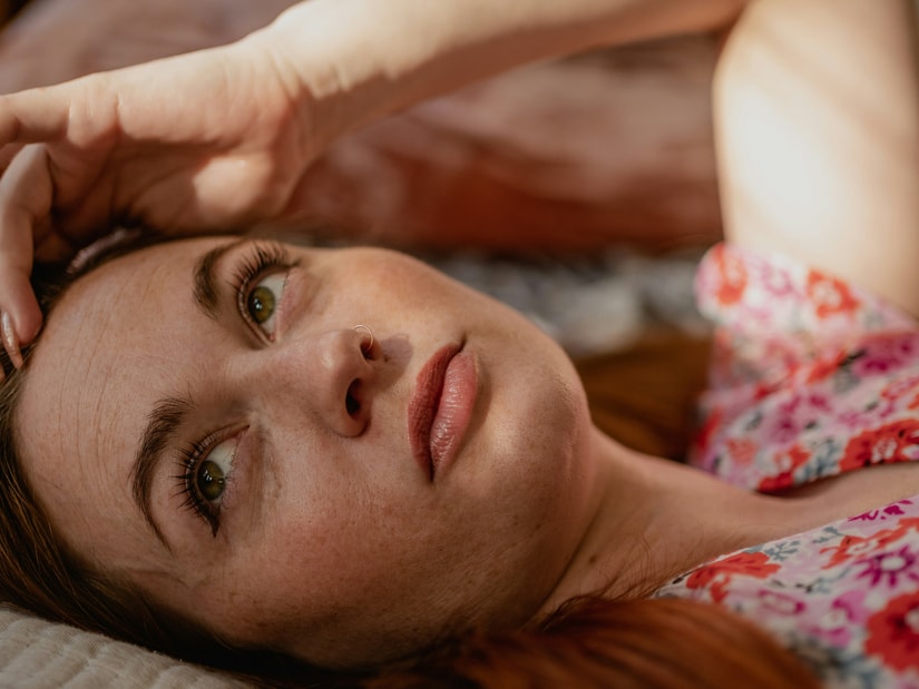 A woman lying on her side on a bed with one hand resting against her temple
