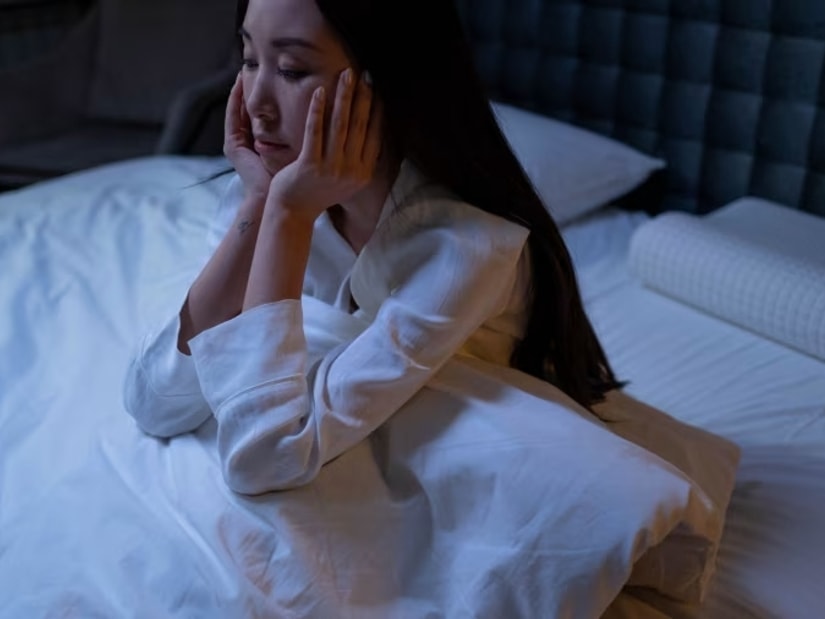 A woman lying awake in bed in dim light with her hands resting against her face
