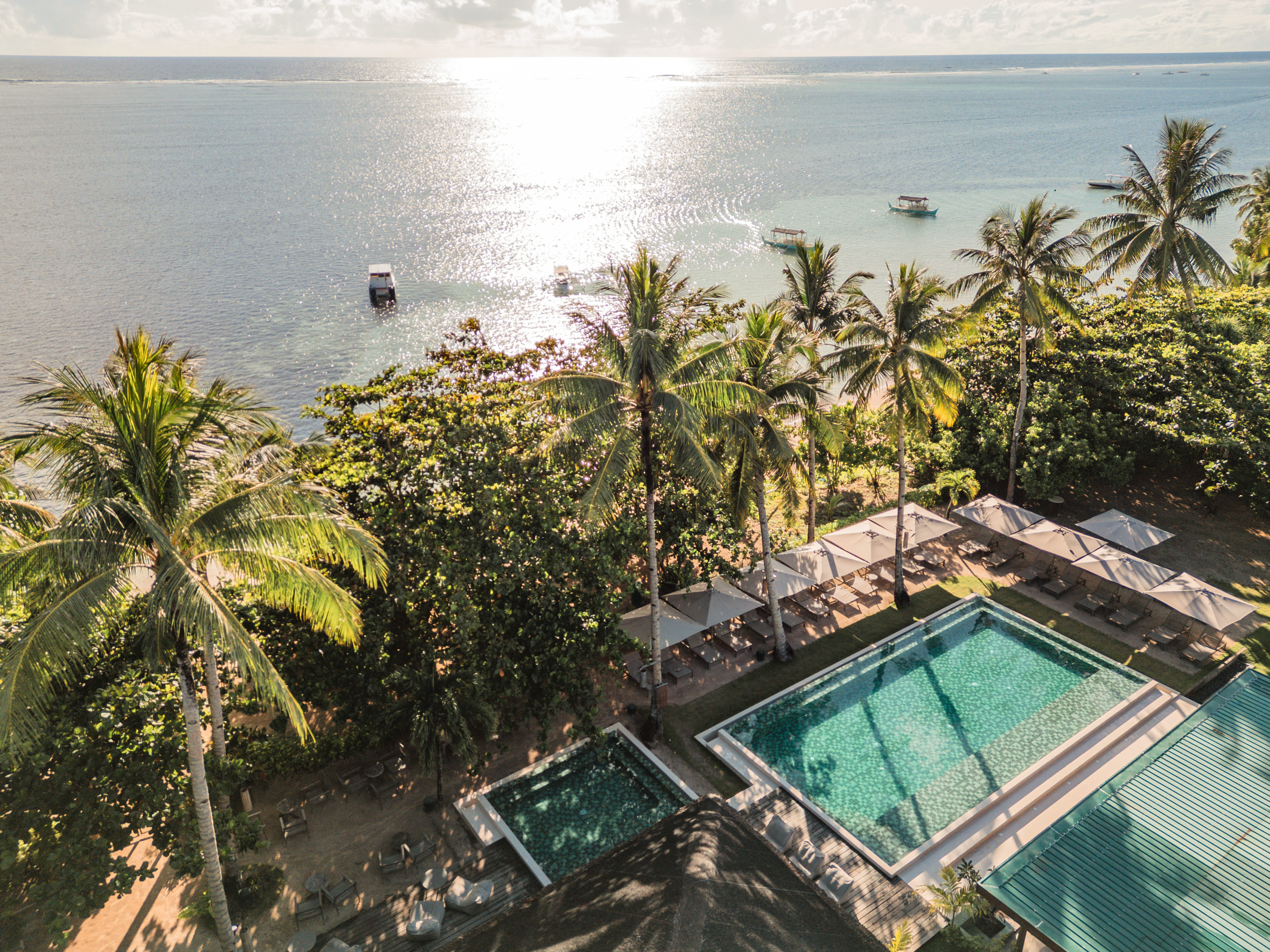 Aerial view of the pool and palm-lined beach with boats at Bravo Beach Resort Siargao
