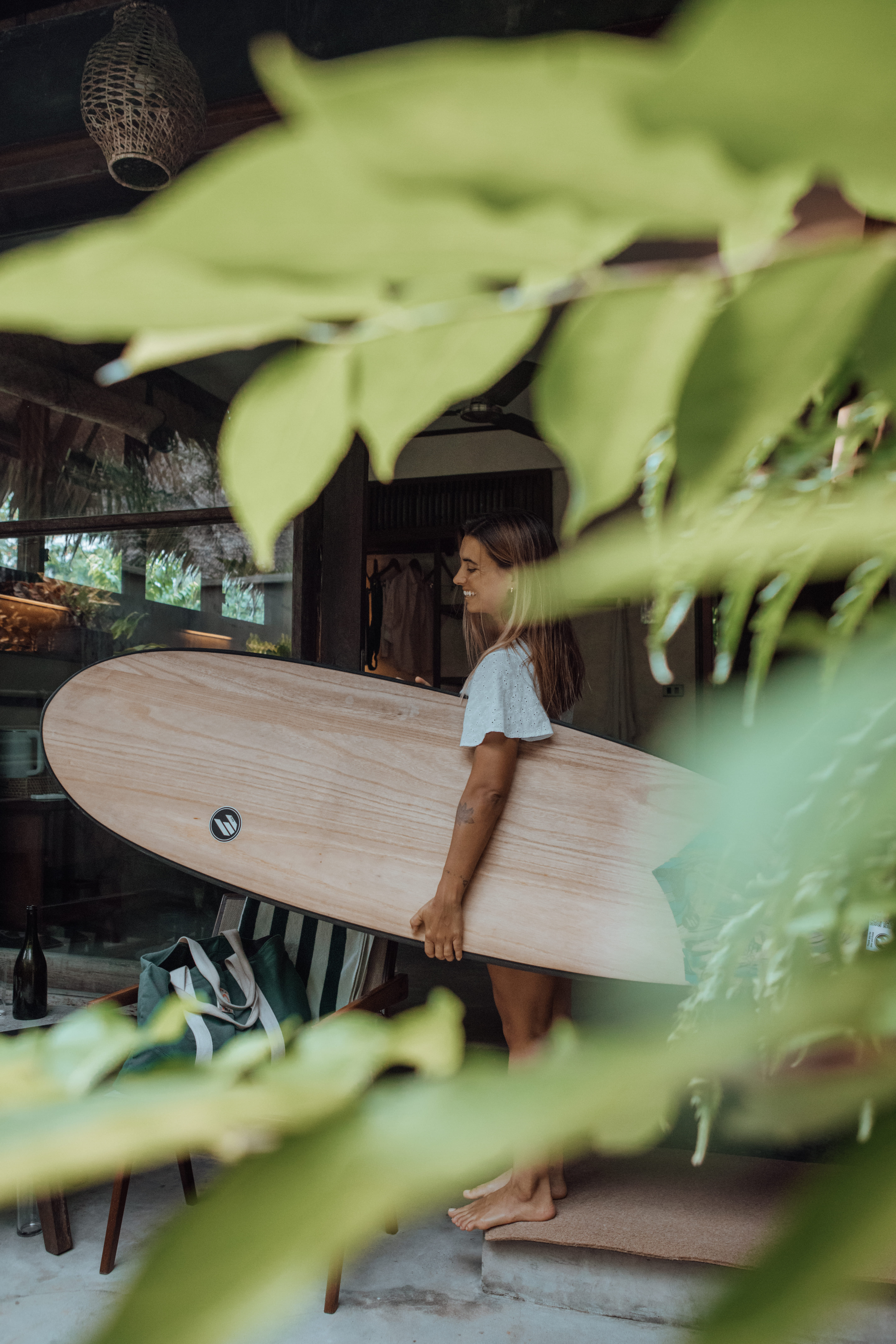 Woman smiling while carrying a surfboard near the villa entrance at Bravo Beach Resort Siargao