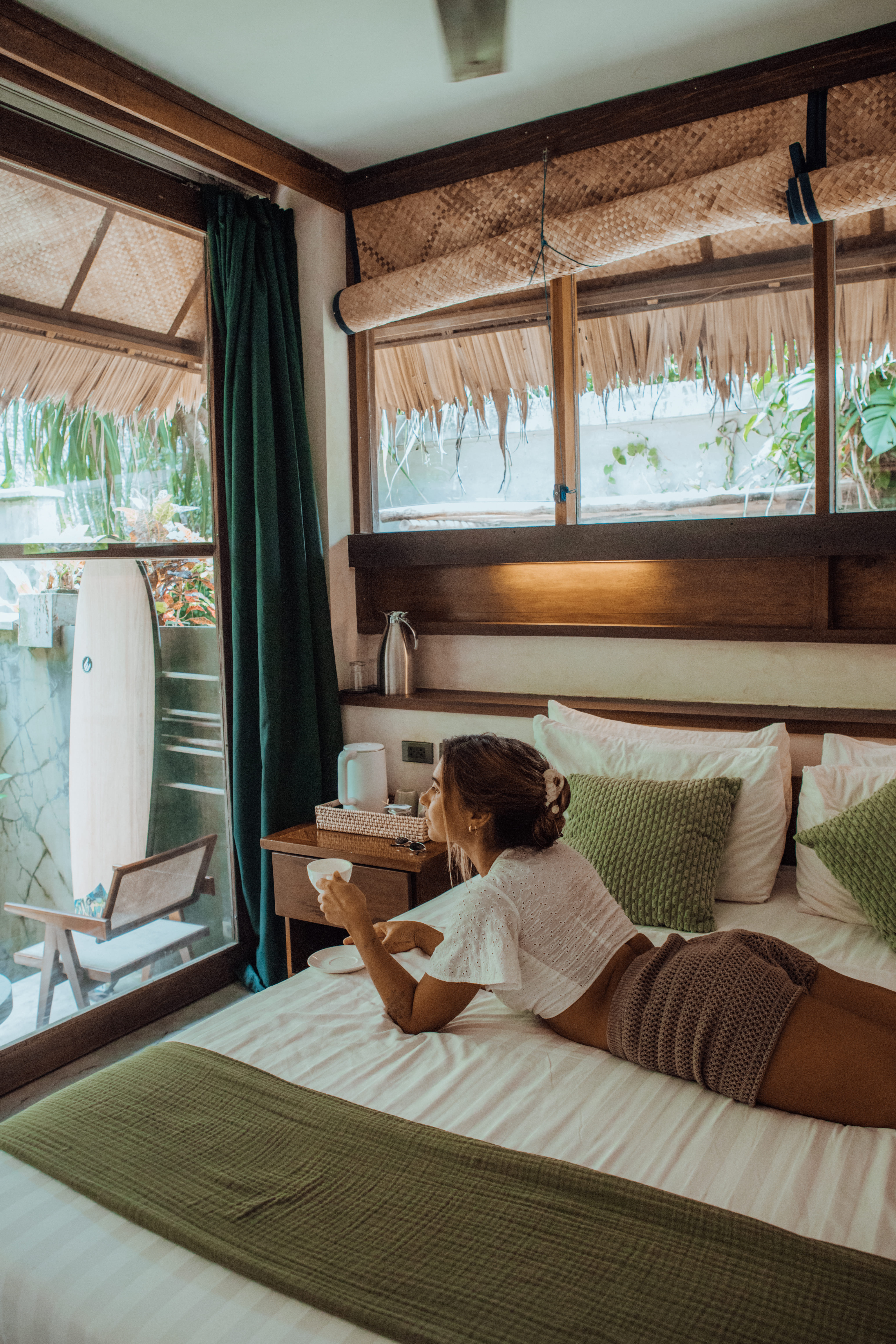 Guest room with a wooden bed, white bedding, and a surfboard leaning against the wall at Bravo Beach Resort Siargao