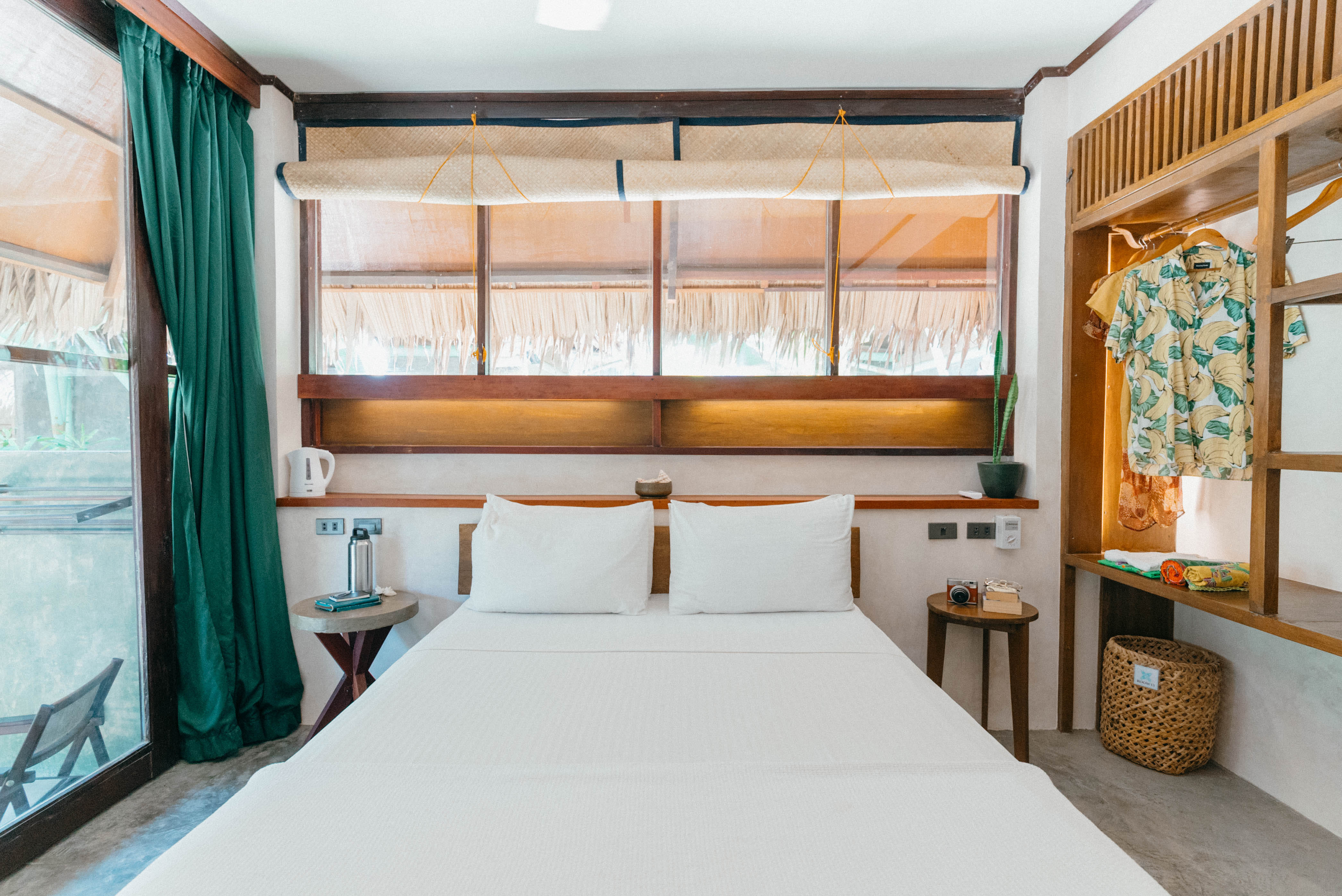 The Garden Room bed at Bravo Beach Resort Siargao with a bamboo blind headboard and a shirt hanging nearby