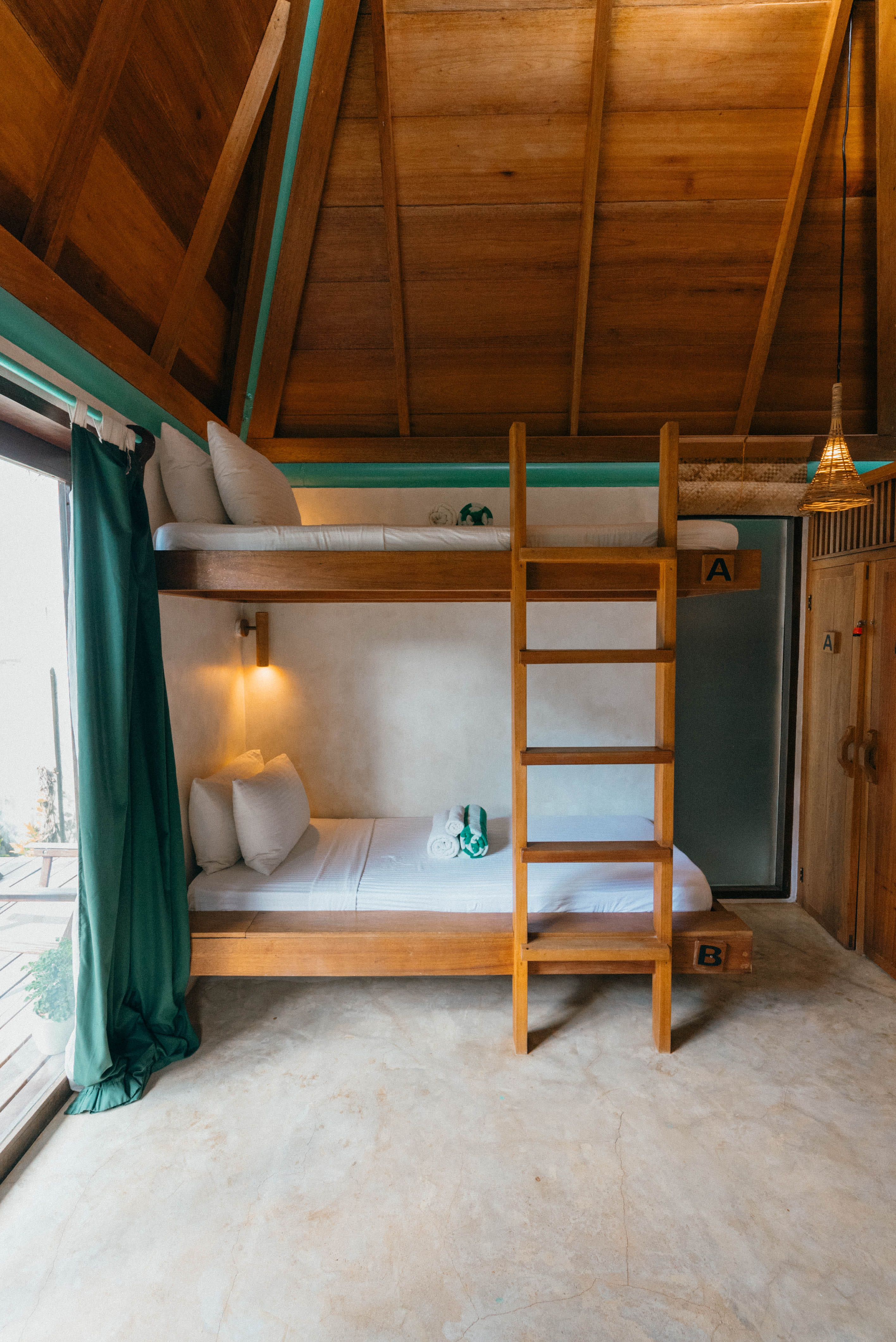 Bunk beds beneath the A-frame roof of the Surf Shack at Bravo Beach Resort Siargao, with a wooden ladder and green curtain