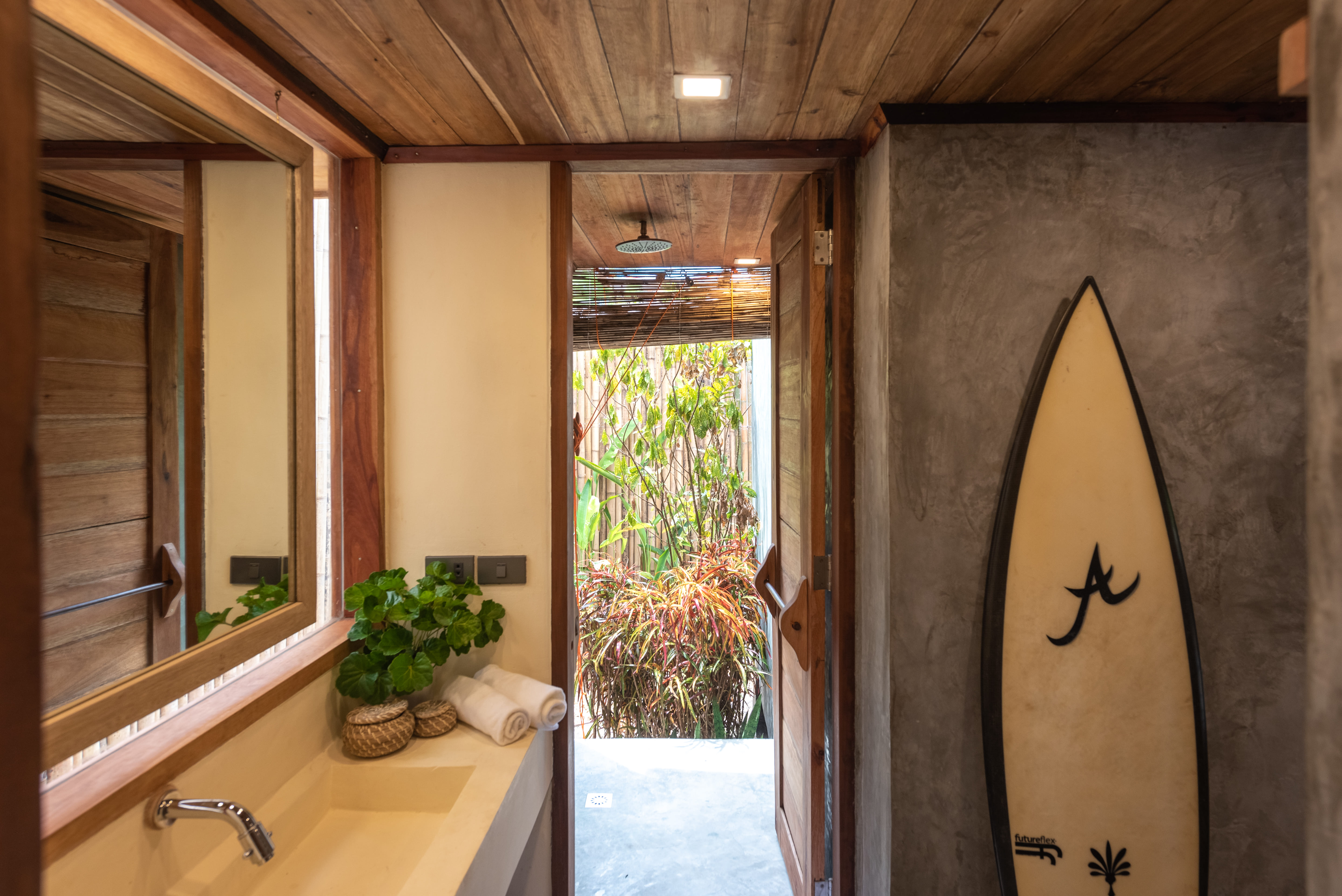 The bathroom vanity at Tadhana Villa, Bravo Beach Resort Siargao, with a surfboard in an alcove beside the garden door