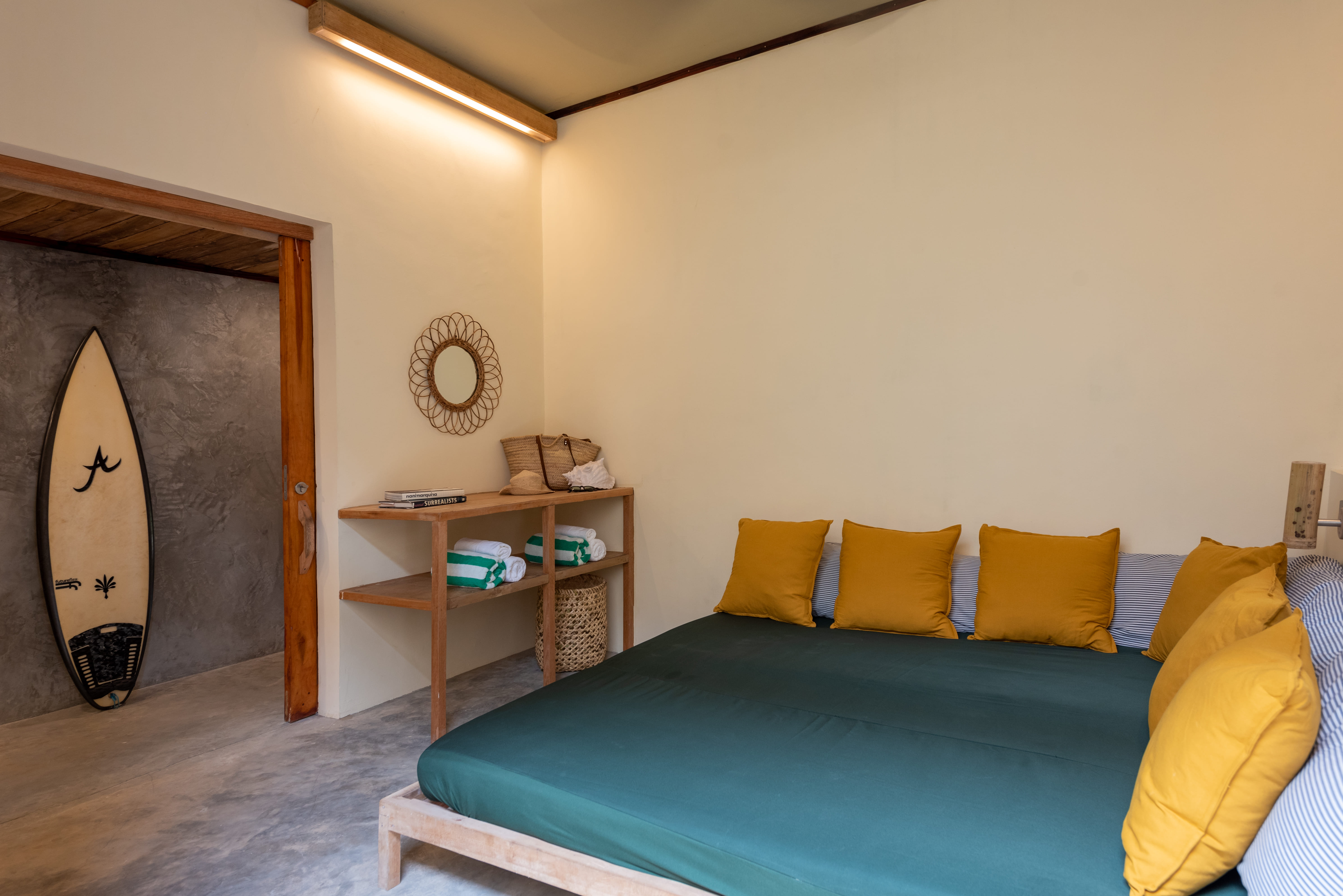 A lounge corner at Tadhana Villa, Bravo Beach Resort Siargao, with a surfboard and a teal bedspread with pillows