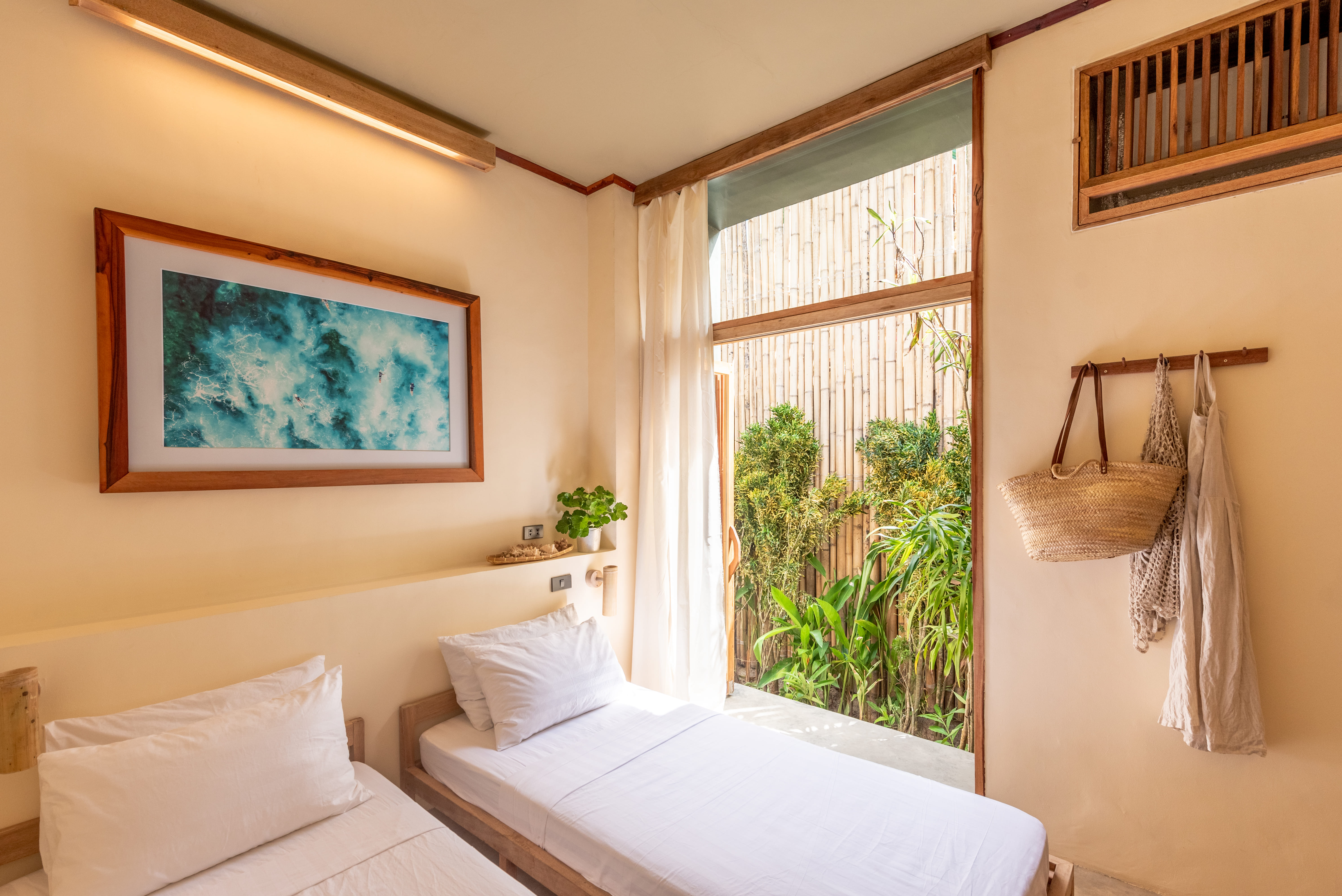 Twin beds at Tadhana Villa, Bravo Beach Resort Siargao, beneath a framed wave photo with a tote bag hanging nearby