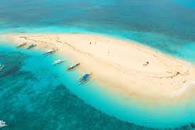 Aerial view of a small white sandbar island known as Naked Island in Siargao, with outrigger boats moored along its turquoise edges